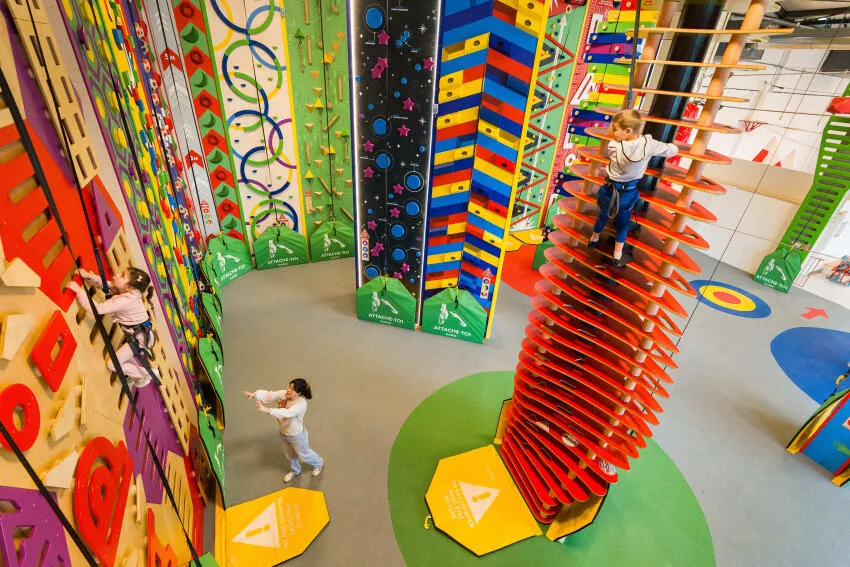 des enfants grimpent des murs d'escalade thématiques et colorés accompagnés de leur maman